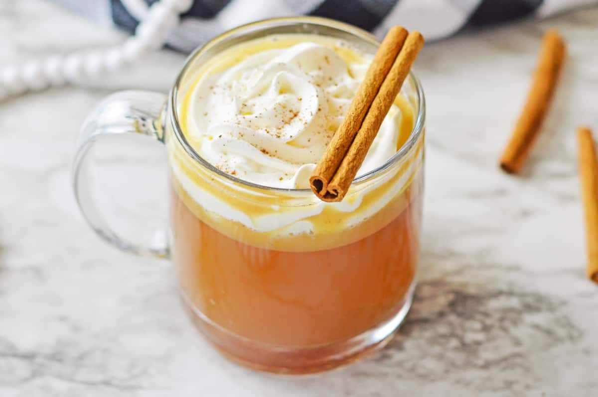 Old-fashioned hot buttered rum served in a glass cup with whipped cream and a cinnamon stick. 