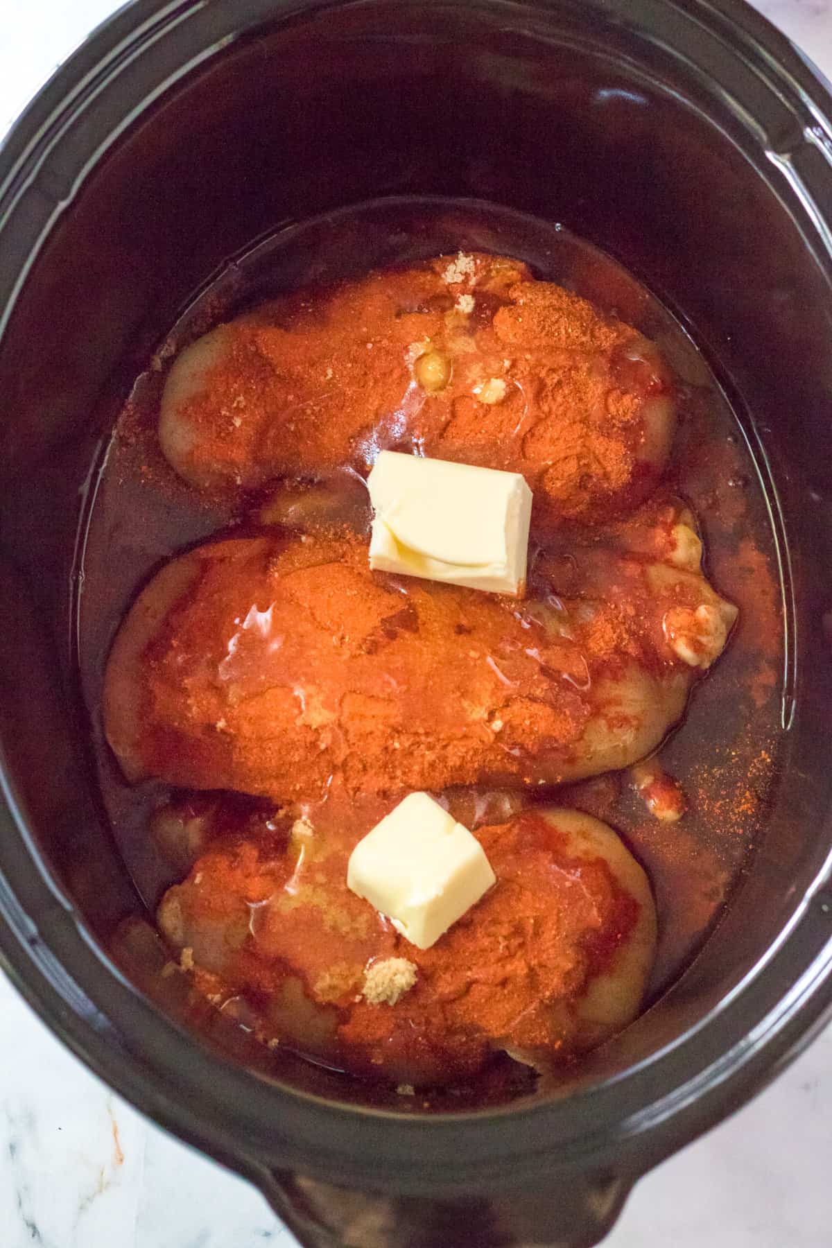 Chicken breasts and hot honey sauce ingredients in the bottom of a crockpot.