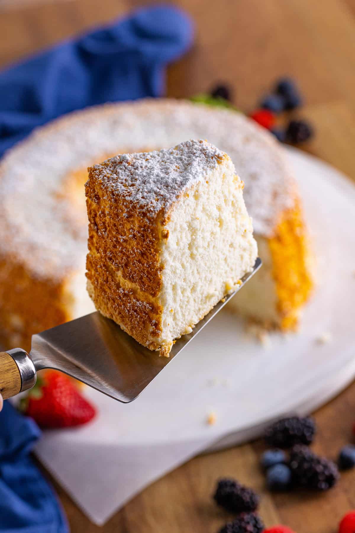 Slice of angel food cake being lifted from rest of cake with a silver cake server.