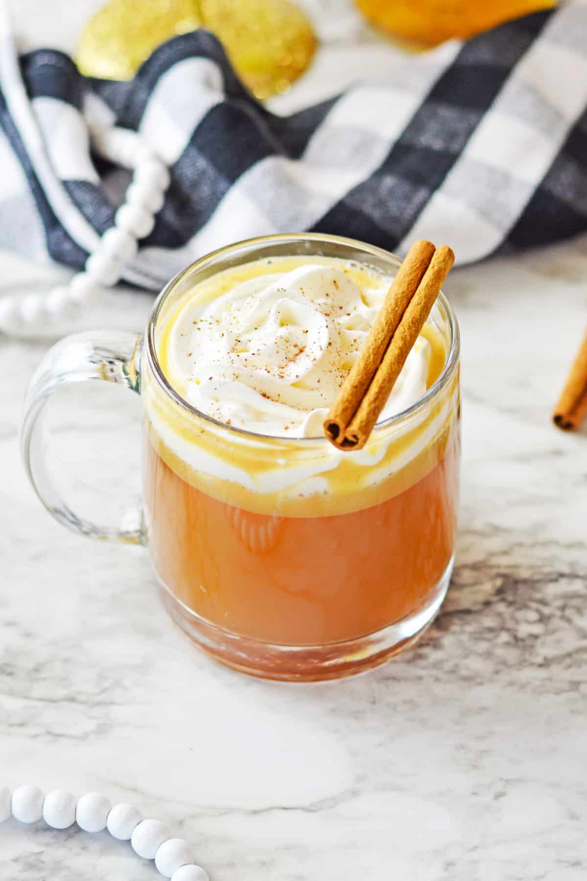 Hot buttered rum cocktail topped with whipped cream and cinnamon stick in a clear glass mug.