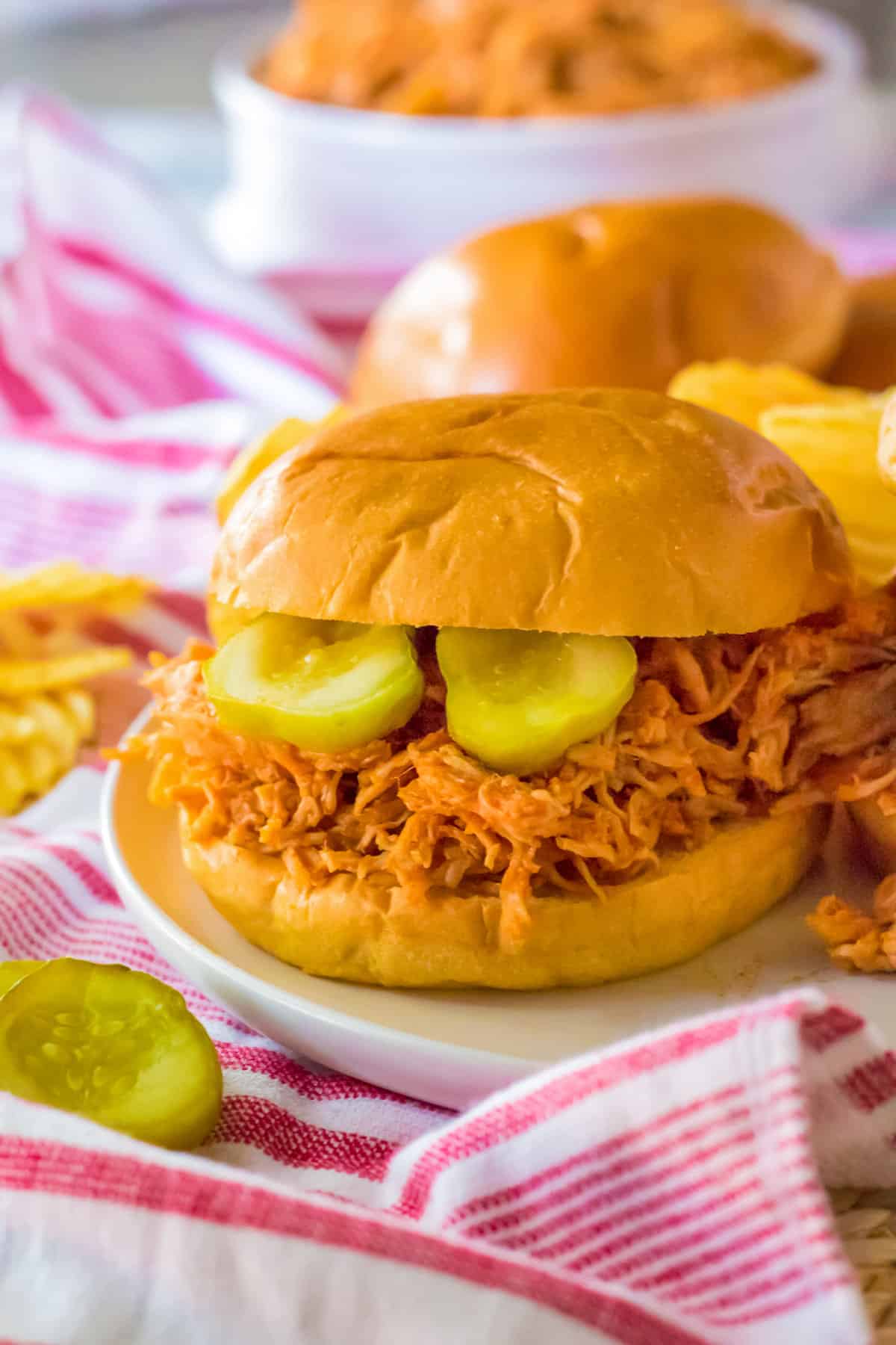 Slow cooker hot honey chicken sandwich served on a soft bun with pickles and chips.