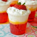 Strawberries and cream jello shots with 3 distinct layers: Strawberry jello, vanilla pudding, and whipped cream.