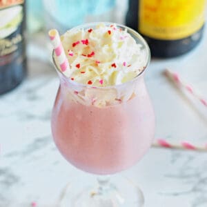 Pink strawberry mudslide in a glass with Kahula and Baileys bottles behind it.