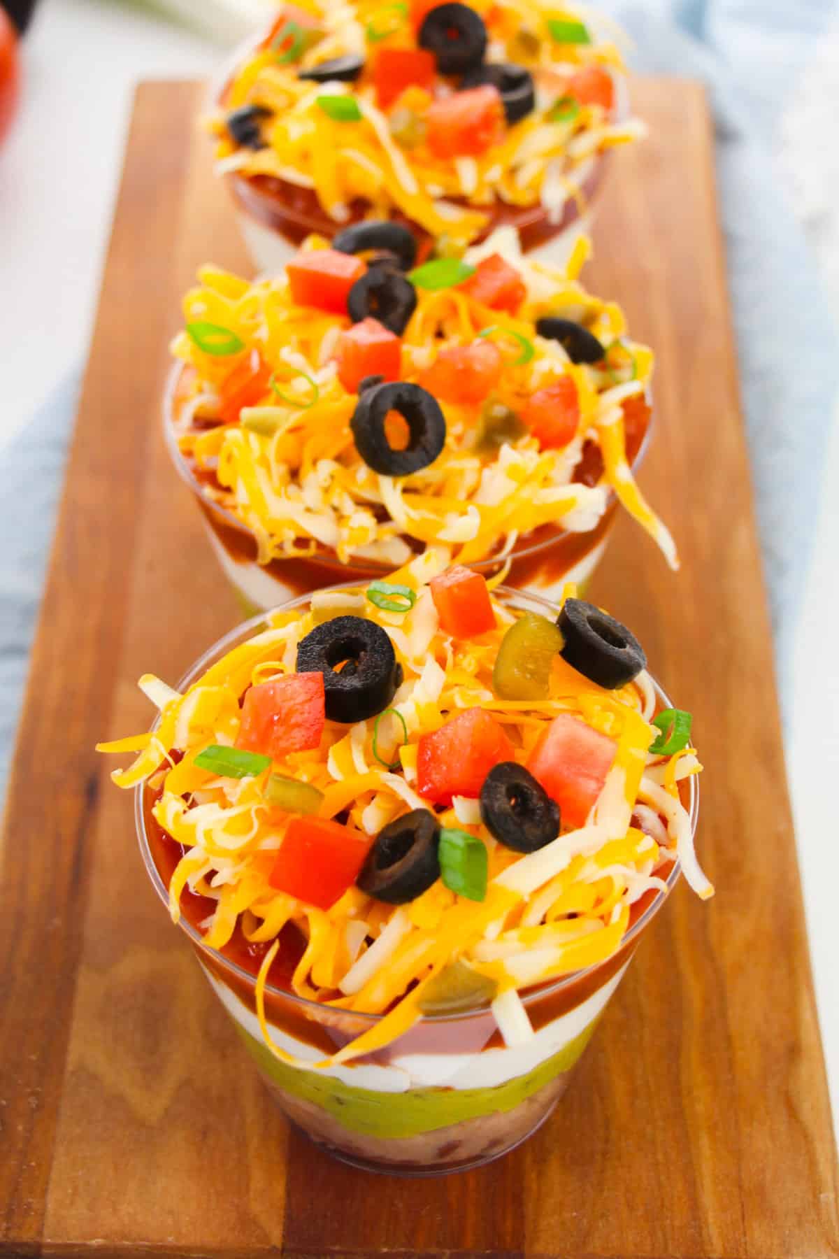 Taco dip in individual cups lined up on serving board.