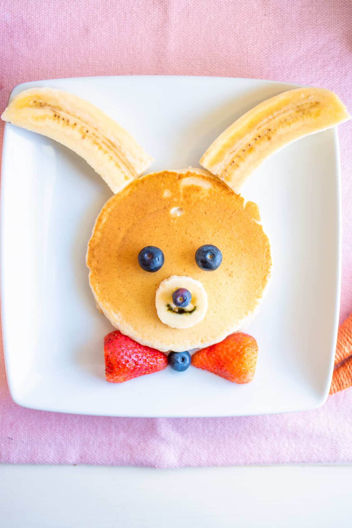 Bunny pancakes made with a large pancake and decorated with banana, strawberry, and blueberries.