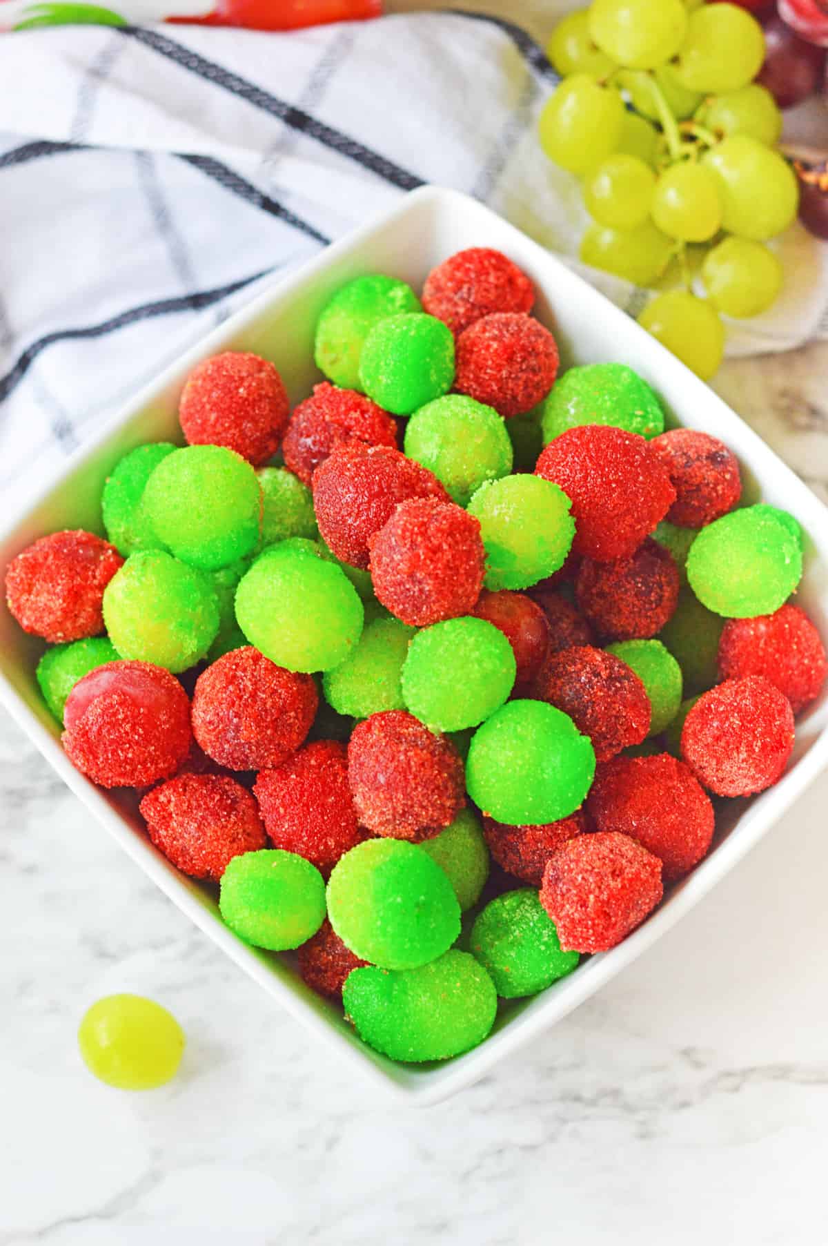 Overhead image of strawberry and green apple candied grapes in a white bowl.