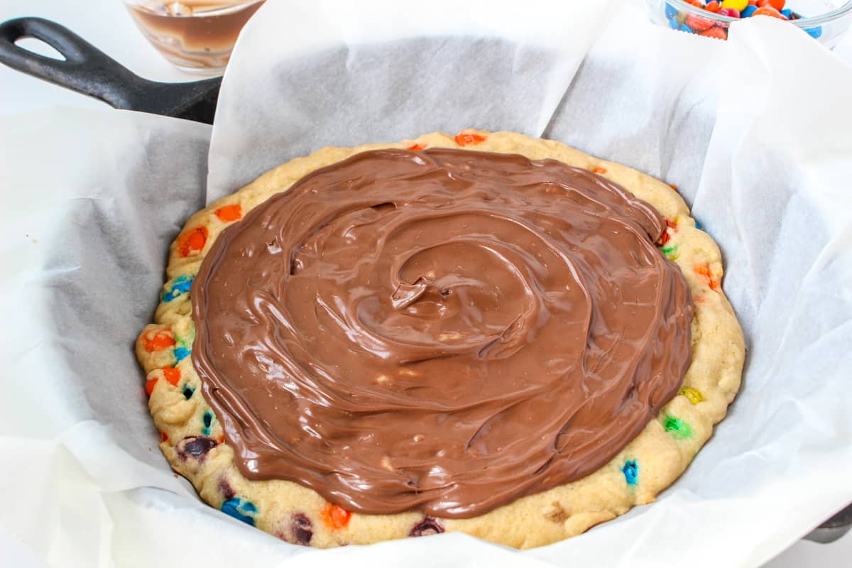 Skillet cookie topped with melted chocolate, leaving the edge uncovered similar to a pizza crust.
