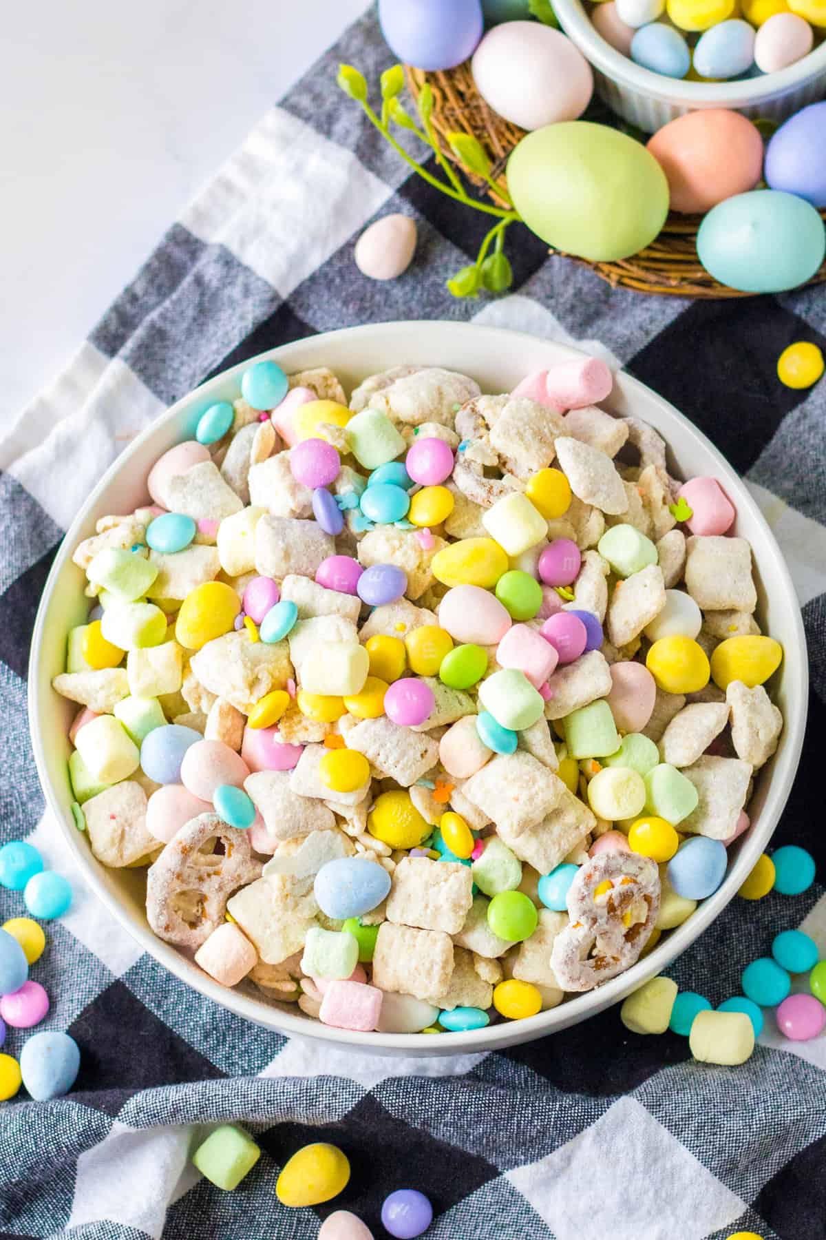 Easter snack mix in a large white serving bowl surrounded by Easter candies and egg decorations.