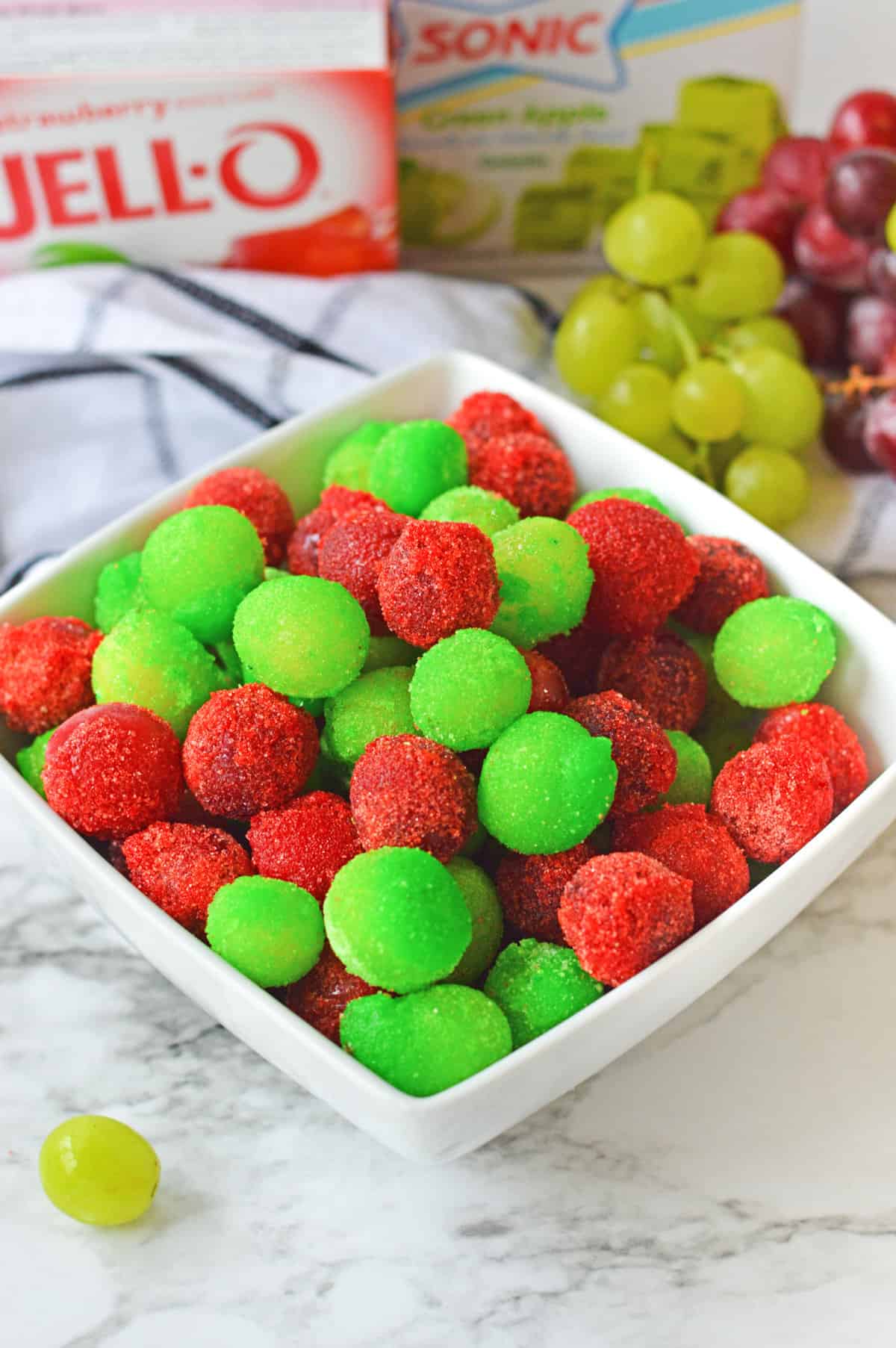 Candied grapes with jello powder in a bowl with fresh grapes and jello mix in the background.