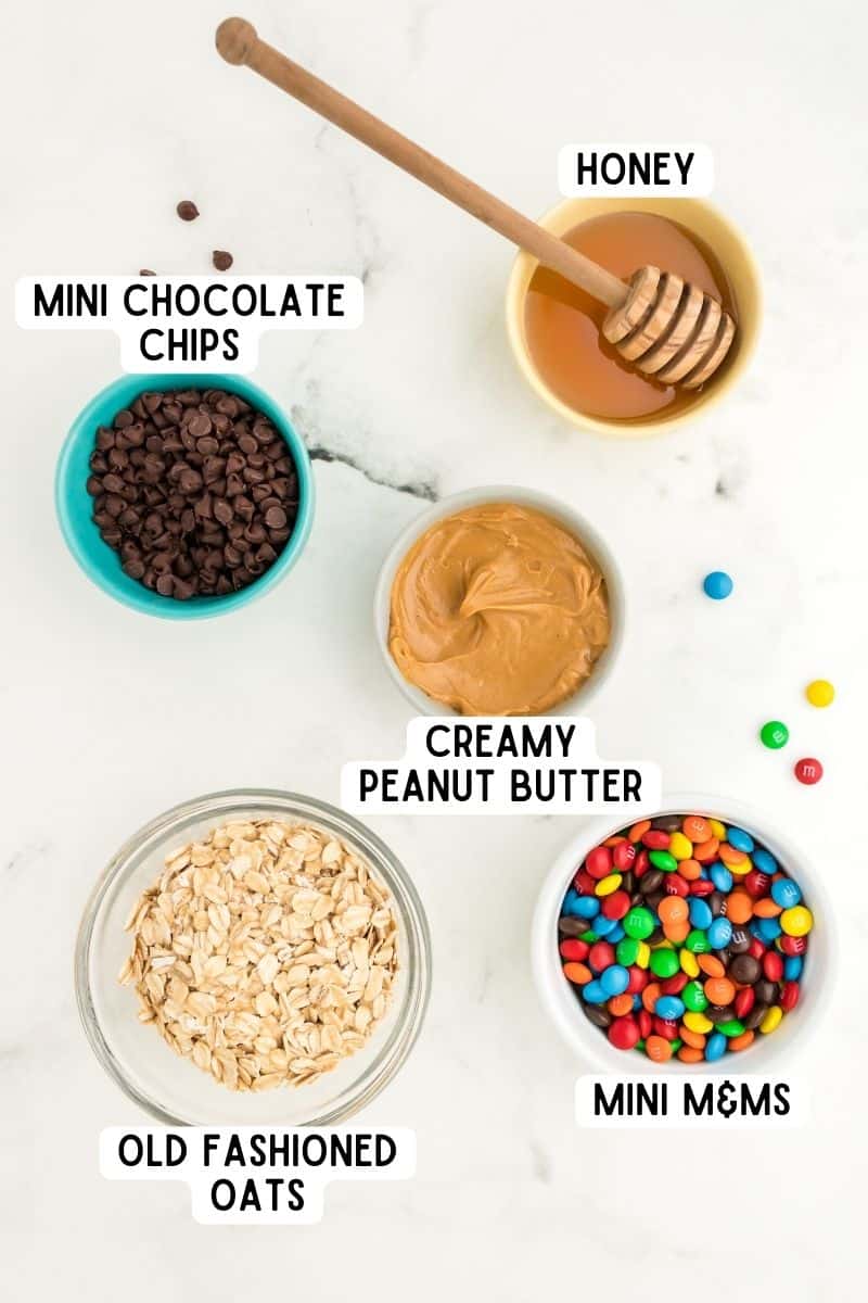 Ingredients in bowls: honey, creamy peanut butter, mini chocolate chips, mini M&Ms, and old-fashioned oats.