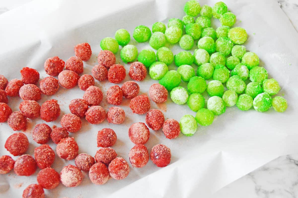 Red and green frozen jello grapes on lines baking sheet.