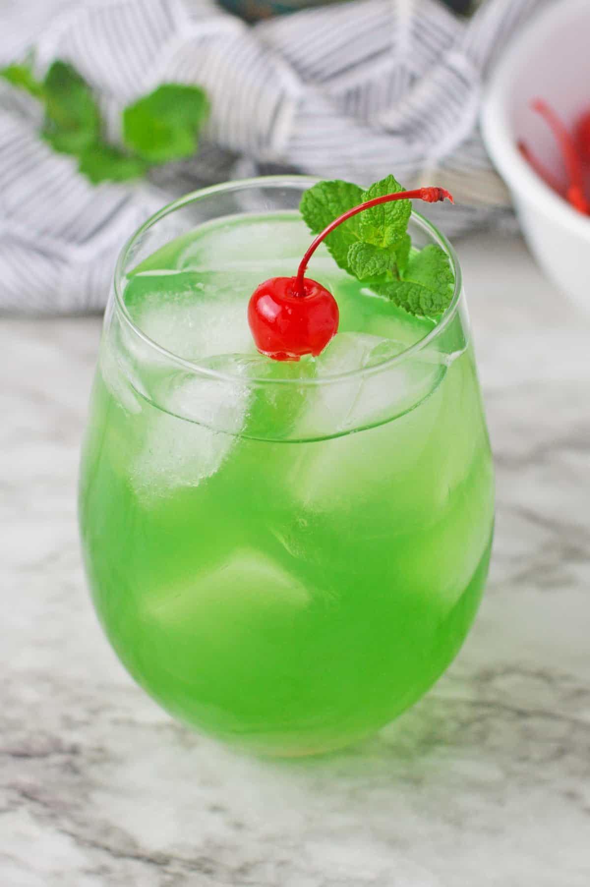 Green cocktail garnished with maraschino cherry and fresh mint.