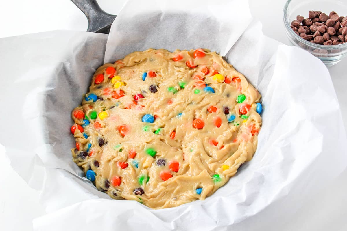 M&M chocolate chip cookie dough in parchment-lined skillet.