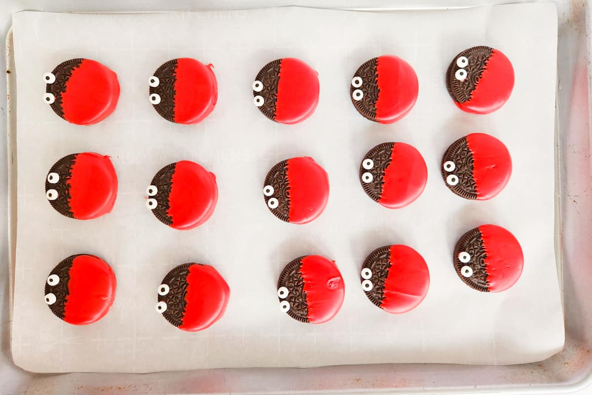 Dipped oreos with candy eyeballs on parchment-lined baking sheet.