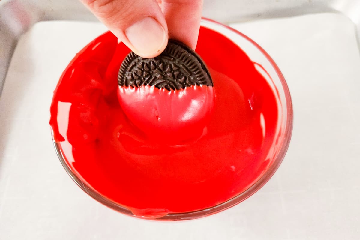 Oreo cookie being dipped in red melted candy.