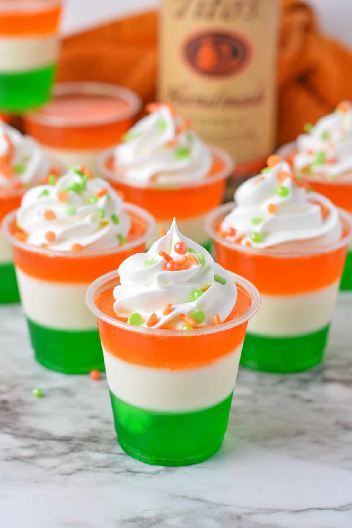 Green, white, and orange layered jello shots with whipped cream and sprinkles.
