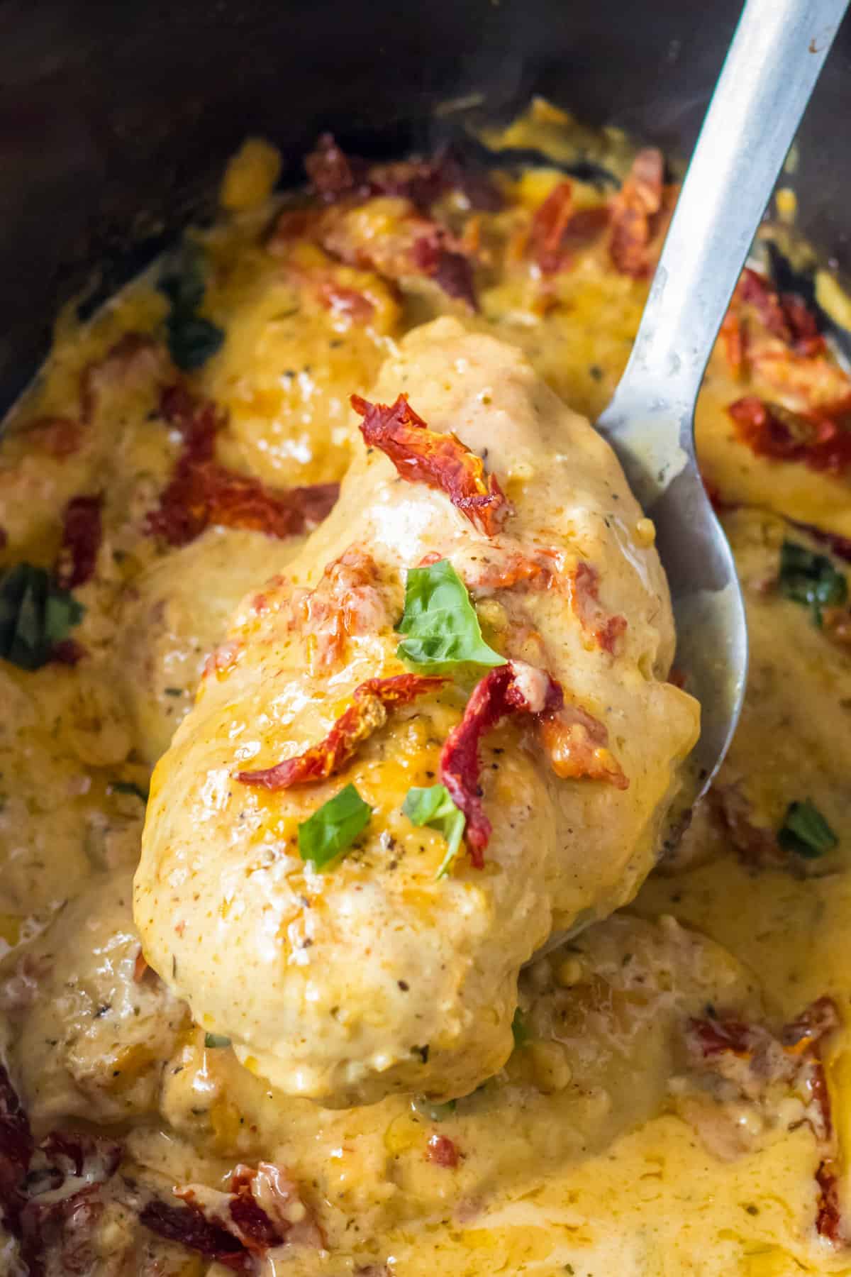 Marry me chicken breast being lifted from slow cooker with a serving spoon.