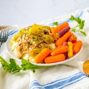 Slow cooker mississipi pork served over mashed potatoes with a side of carrots.