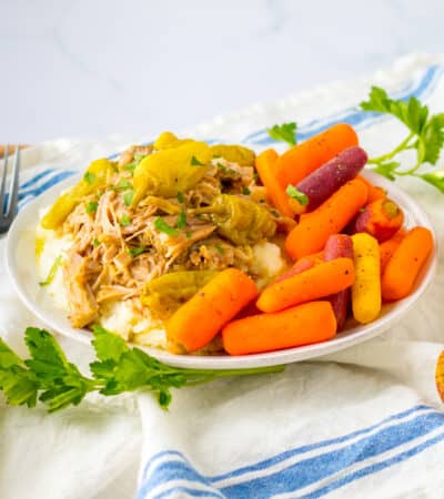Slow cooker mississipi pork served over mashed potatoes with a side of carrots.