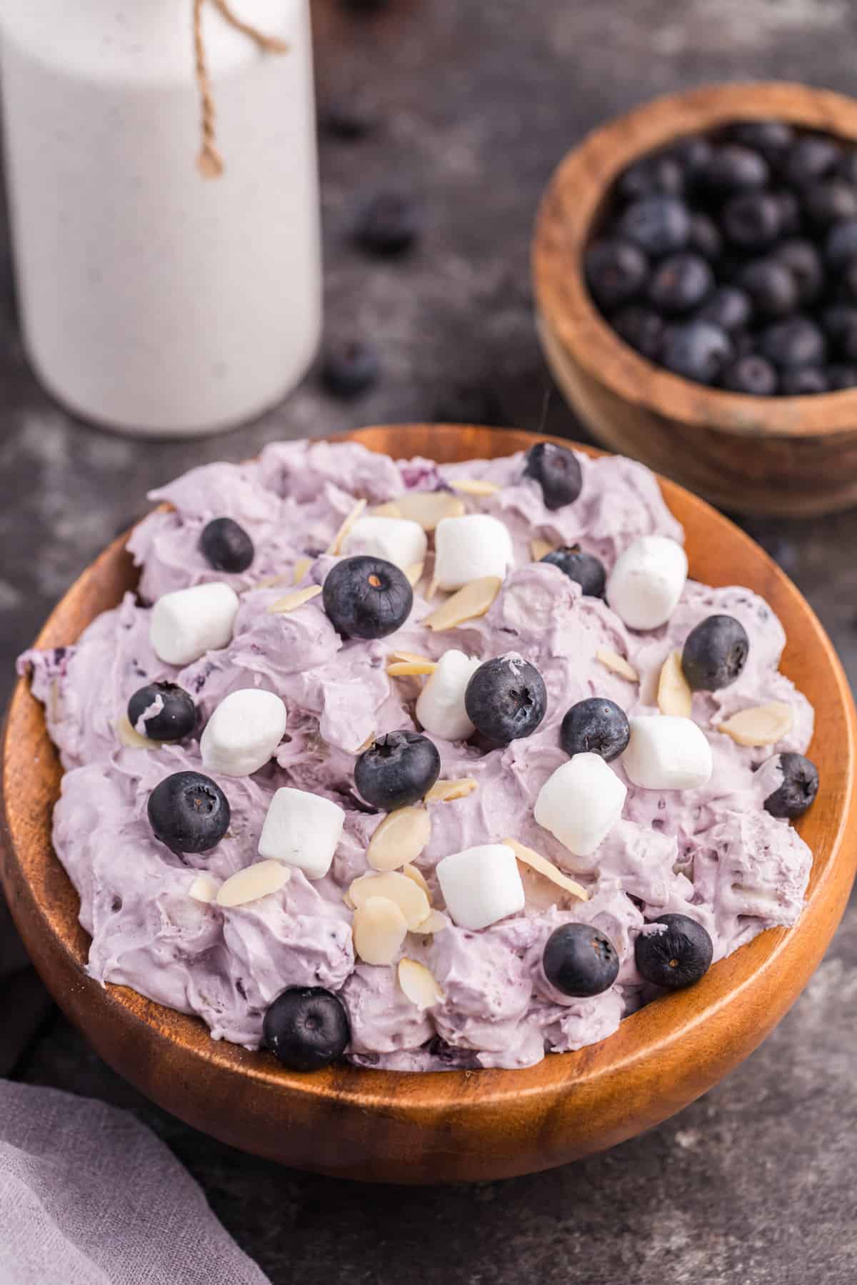 Blueberry fluff salad in a wooden. bowl, topped with mini marshmallows, fresh blueberries, and almond slivers,