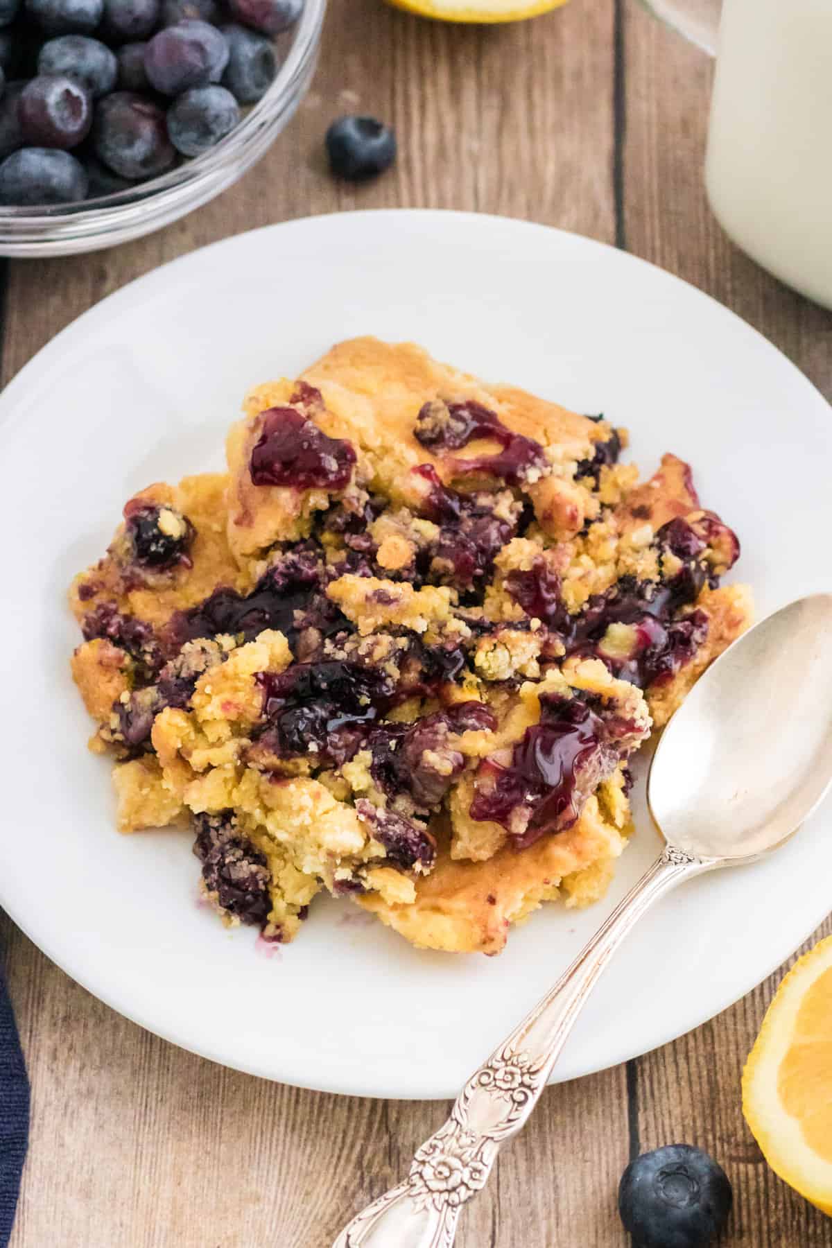 Lemon blueberry dump cake served on a white plate with a silver spoon and milk.