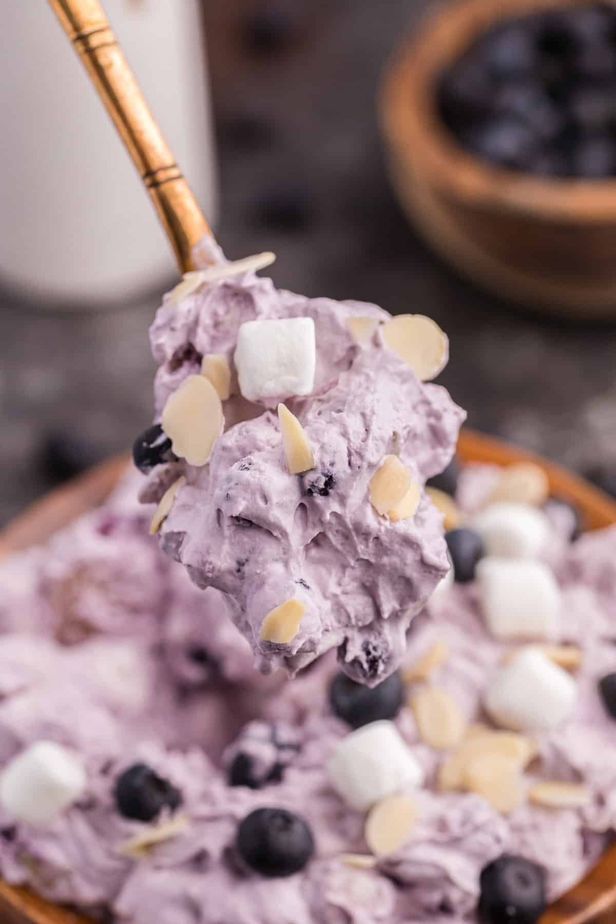 Spoonful of fluffy blueberry salad being lifted out of bowl.