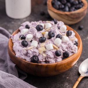 Blueberry fluff salad in a wooden. bowl, topped with mini marshmallows, fresh blueberries, and almond slivers.