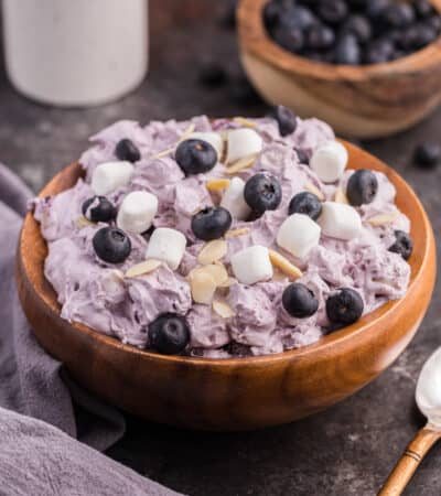Blueberry fluff salad in a wooden. bowl, topped with mini marshmallows, fresh blueberries, and almond slivers.