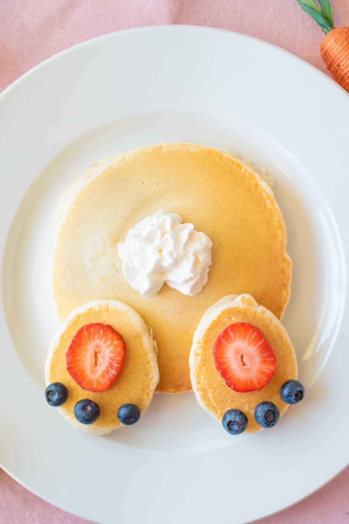 Easter pancakes topped with strawberry slices, blueberries, and whipped cream arranged to look like a bunny's butt.