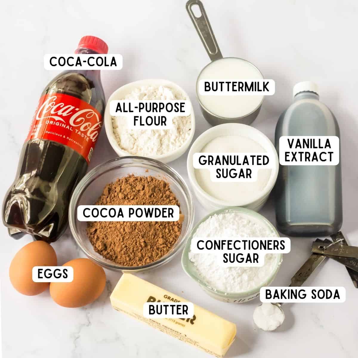 Bottle of Coca-Cola, all-purpose flour, cocoa powder, vanilla extract, buttermilk, stick of butter, baking soda, 2 eggs, granulated sugar, and confectioner's sugar.