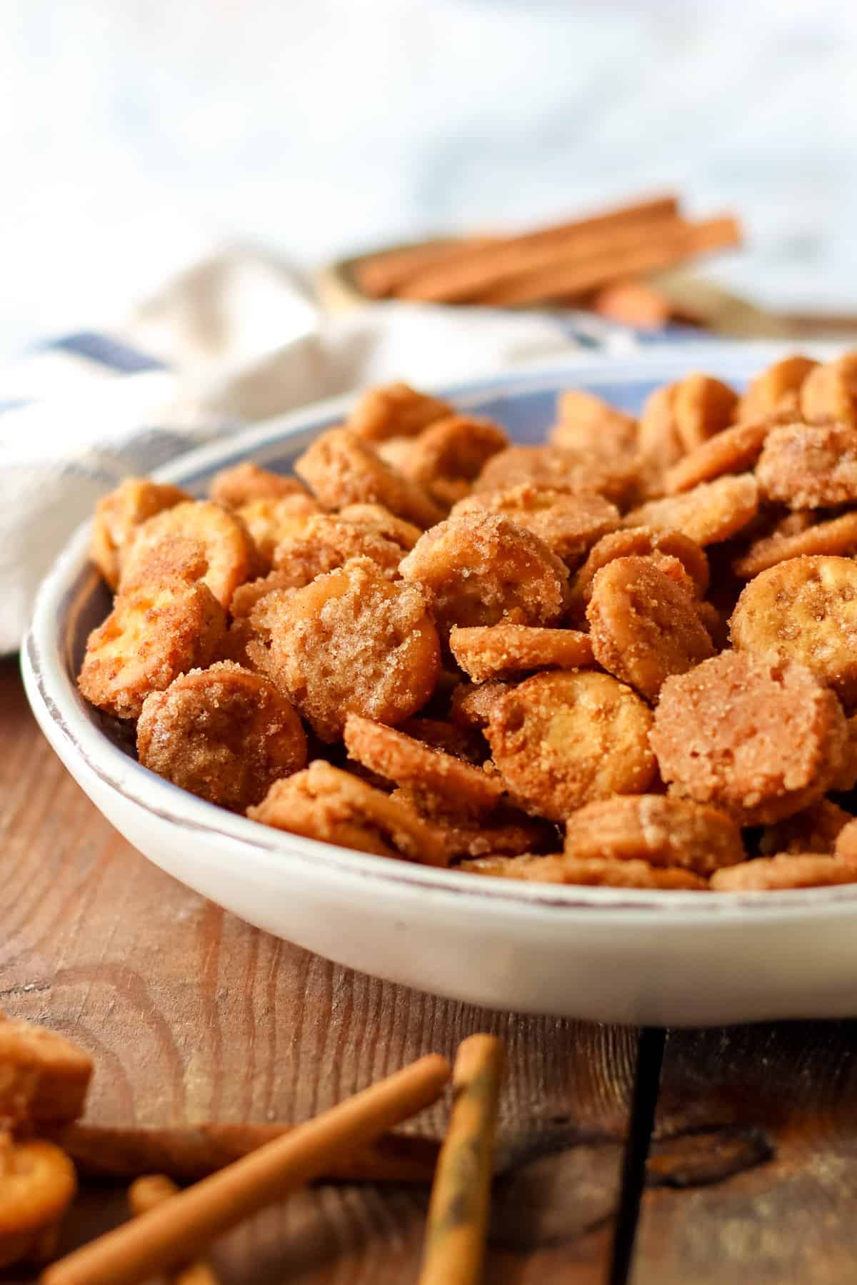 Side view of a bowl of cinnamon sugar coated Ritz Bits with bowl of cinnamon sugar and cinnamon sticks.