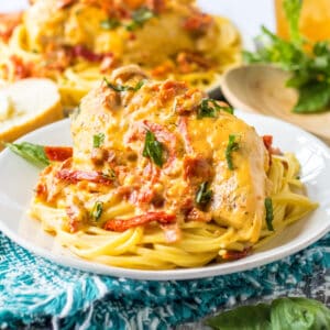 Slow cooker marry me chicken breasts with creamy sun-dried tomato sauce and fresh basil over spaghetti.