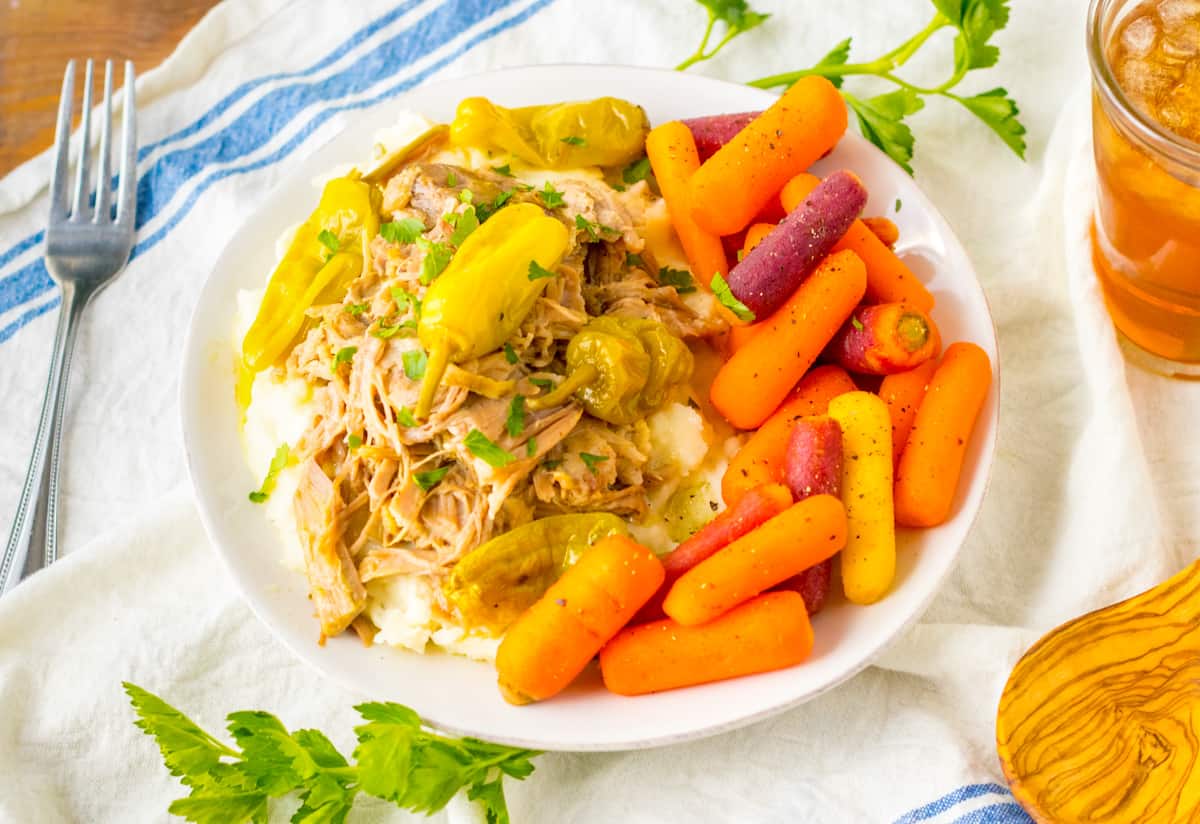 Slow cooker mississipi pork served over mashed potatoes with a side of carrots. 