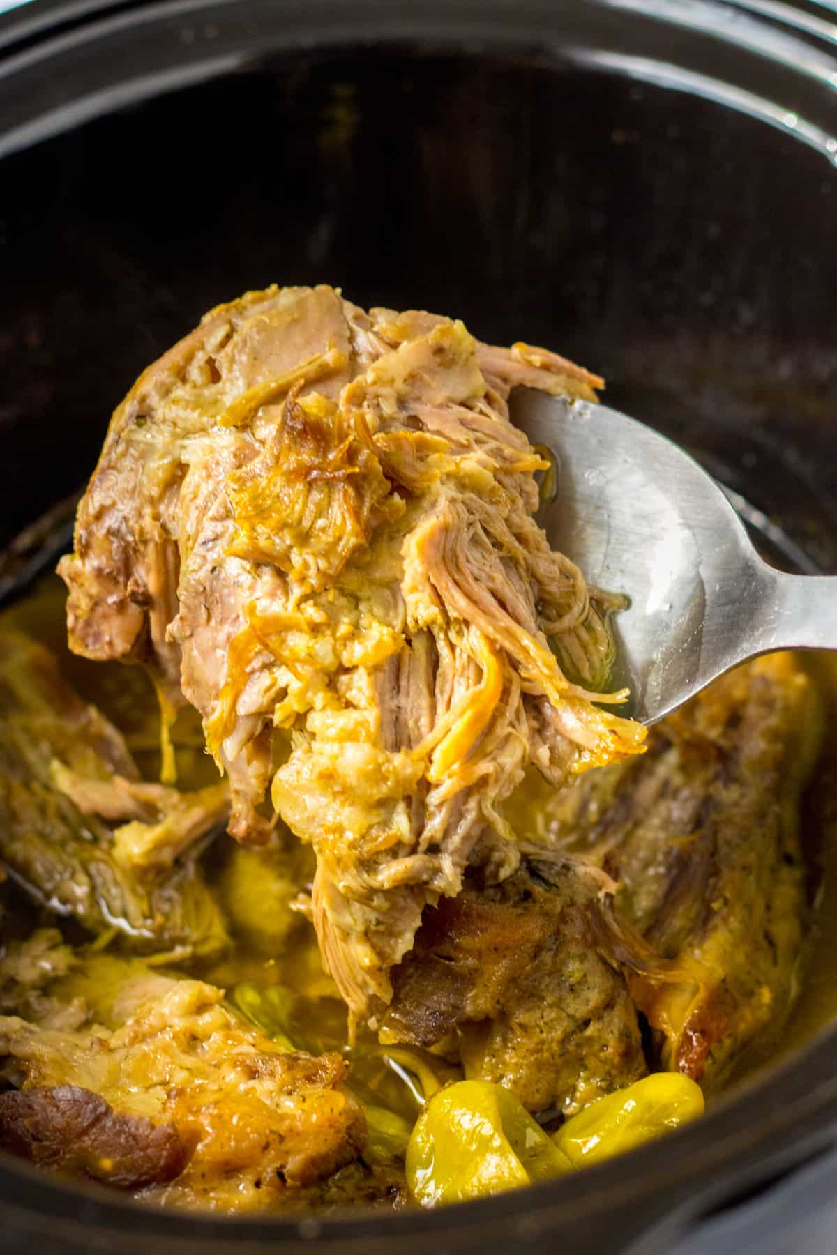 Juicy mississippi pork roast being lifted with a spoon out of the slow cooker. The meat is falling apart it is so unbelievably tender.