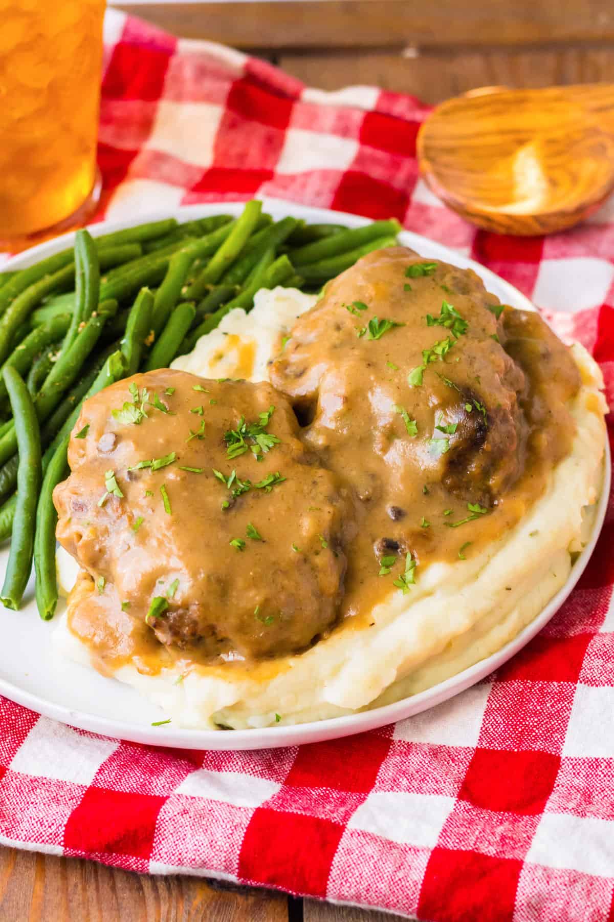 Slow cooker salisbury steaks smothered with brown gravy over a bed of mashed potatoes and served with a side of string beans.