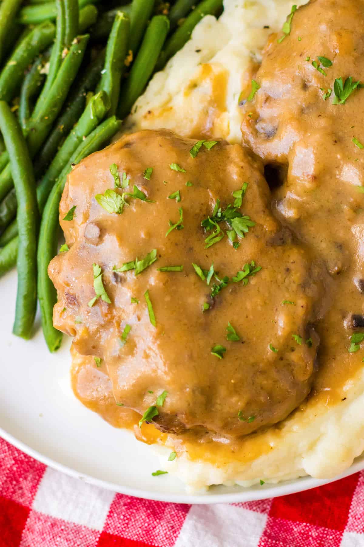 Crockpot salisbury steak with gravy served on a bed of mashed potatoes and garnished with chopped fresh parsley.