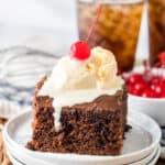 Square slice of chocolate cake with chocolate frosting and scoop of vanilla ice cream and a cherry on top.