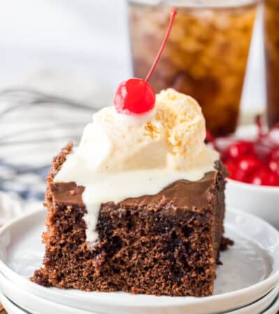 Square slice of chocolate cake with chocolate frosting and scoop of vanilla ice cream and a cherry on top.