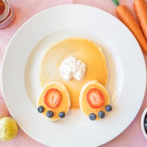 Easter pancakes topped with strawberry slices, blueberries, and whipped cream arranged to look like a bunny's butt.