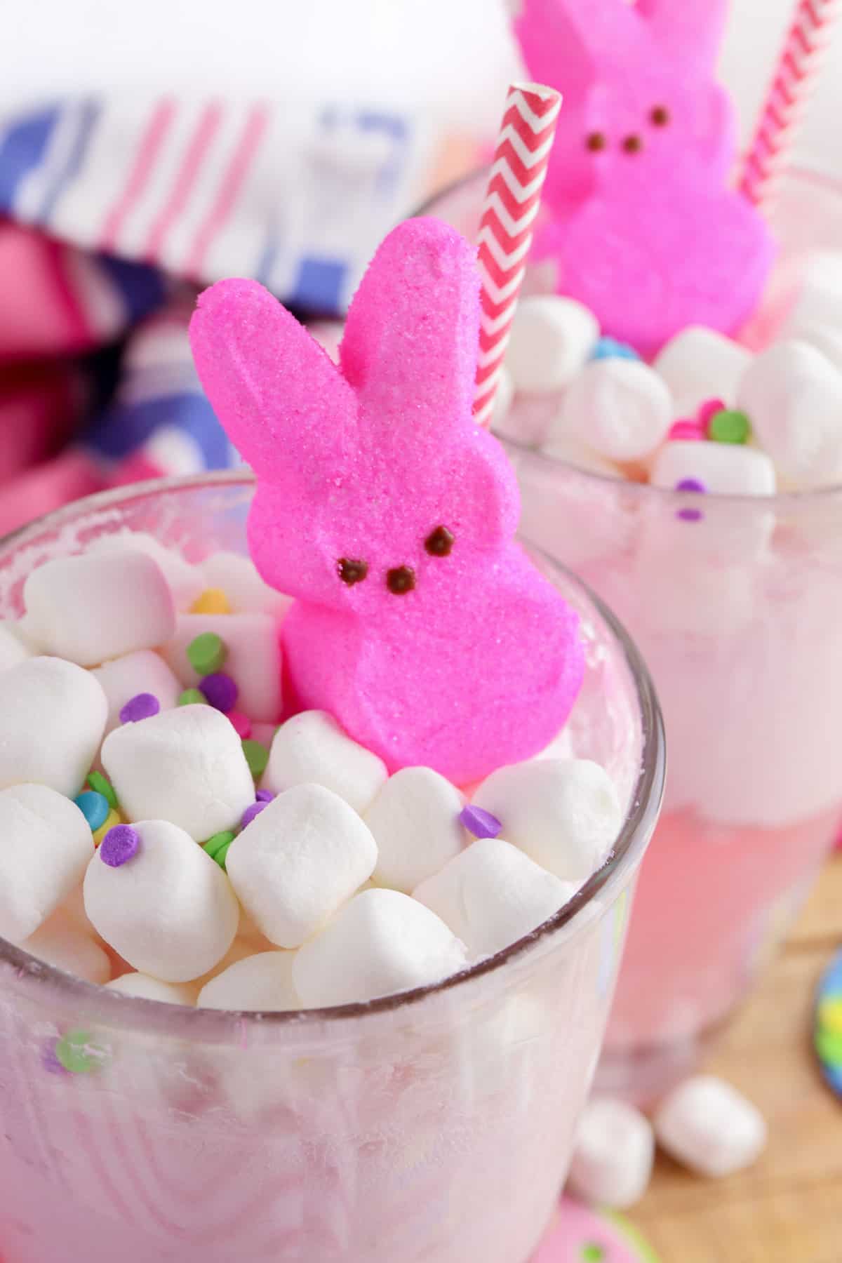 Easter punch in two glasses topped with mini marshmallows, sprinkles, and pink peeps bunnies.