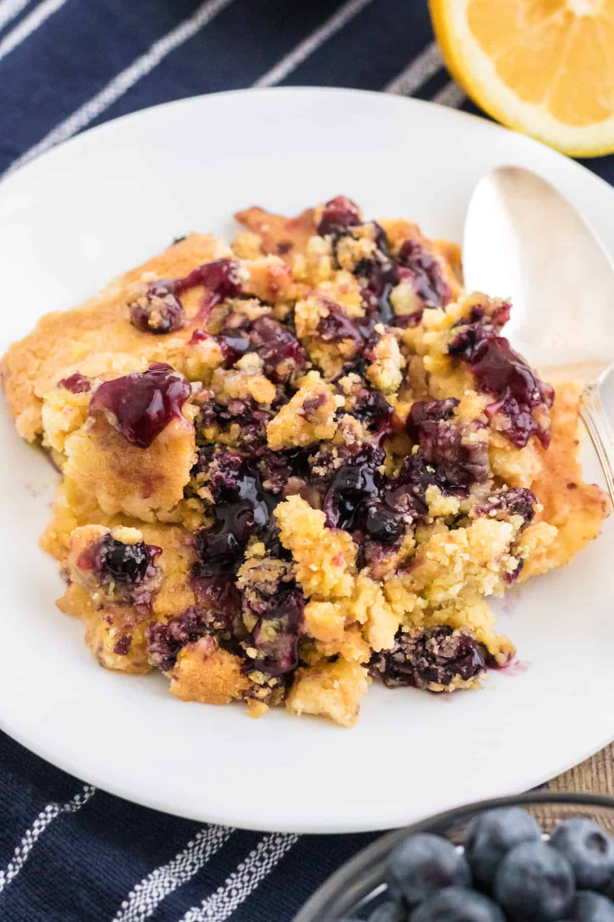 Serving of lemon blueberry dump cake scooped onto on a white plate with a silver spoon.