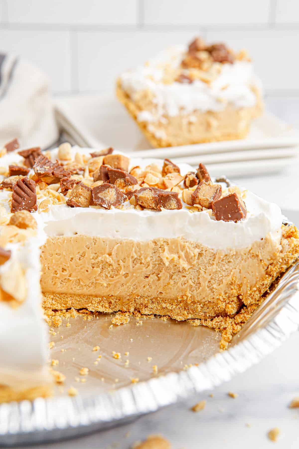 Side-view of peanut butter pie in foil tin with slice removed. You can see distinct layers of creamy peanut butter pie and whipped topping.