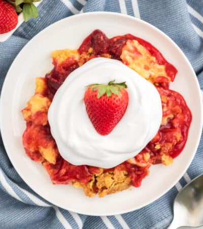 Strawberry dump cake on a white plate topped with cool whip and a fresh strawberry.