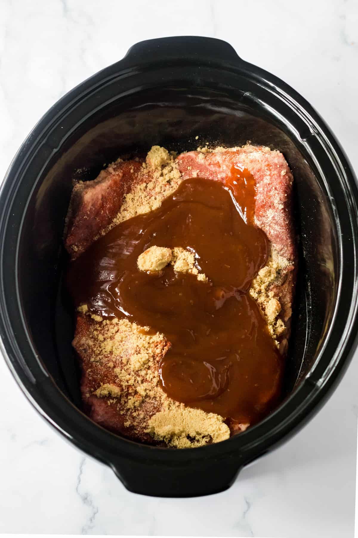 Brisket in slow cooker covered in seasonings and BBQ sauce.