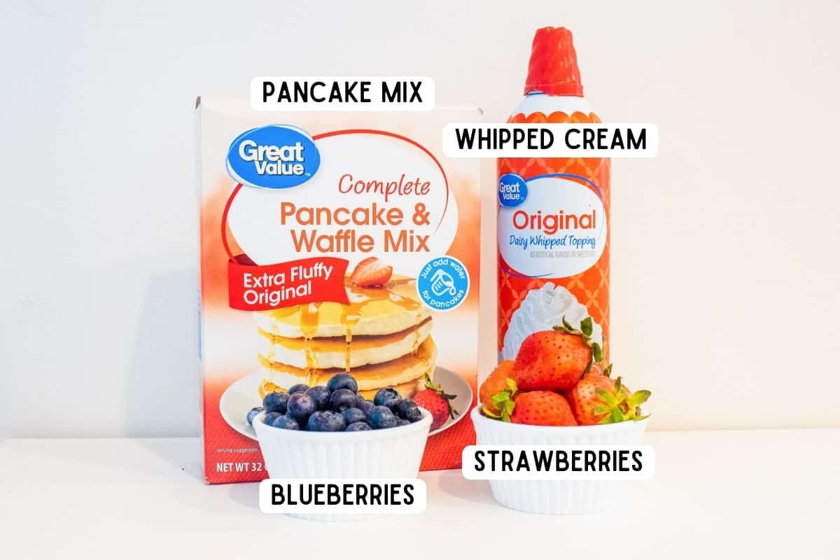 Box of pancake mix, can of whipped cream, bowl of blueberries, bowl of strawberries.
