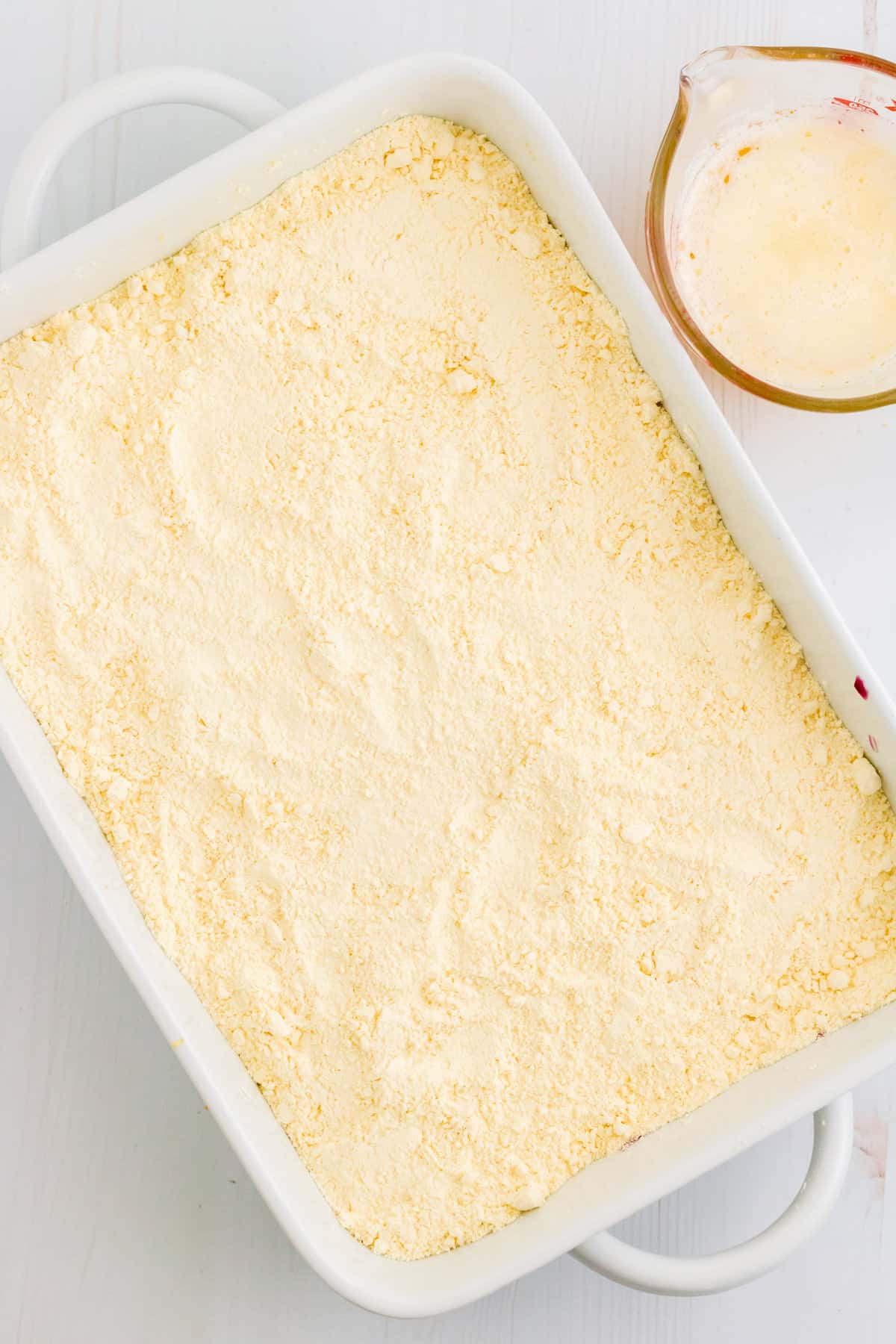The pie filling in the dish has been completely covered with dry lemon cake mix.
