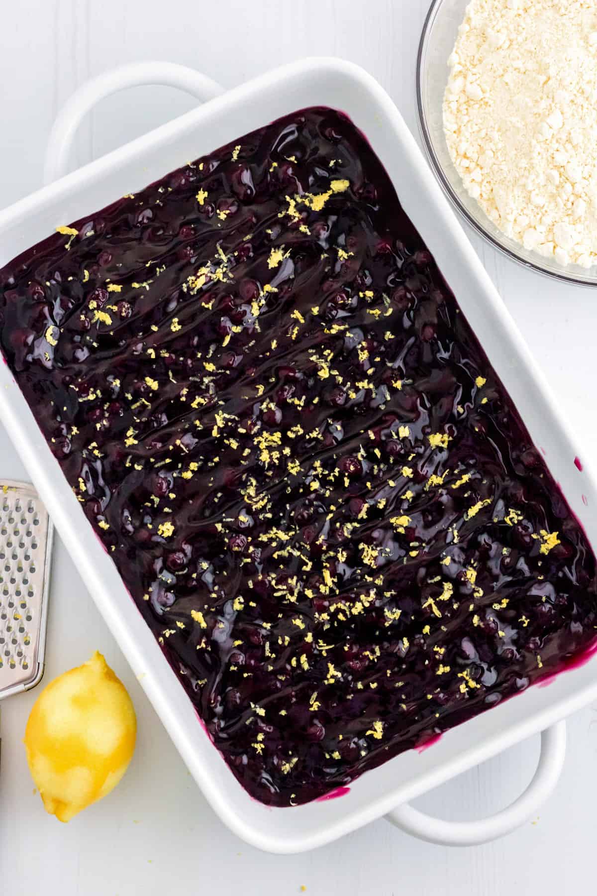 Blueberry pie filling topped with lemon zest in a white baking dish.