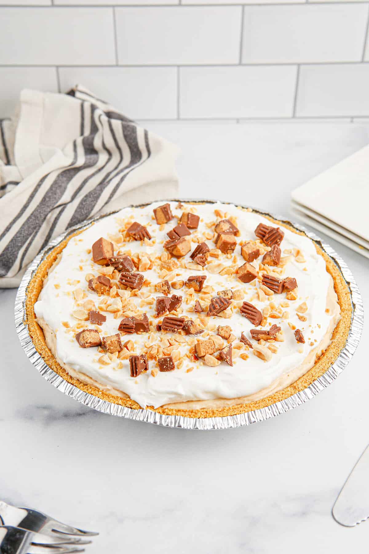 No bake peanut butter pie topped with whipped topping, reese's peanut butter cups, and peanuts.