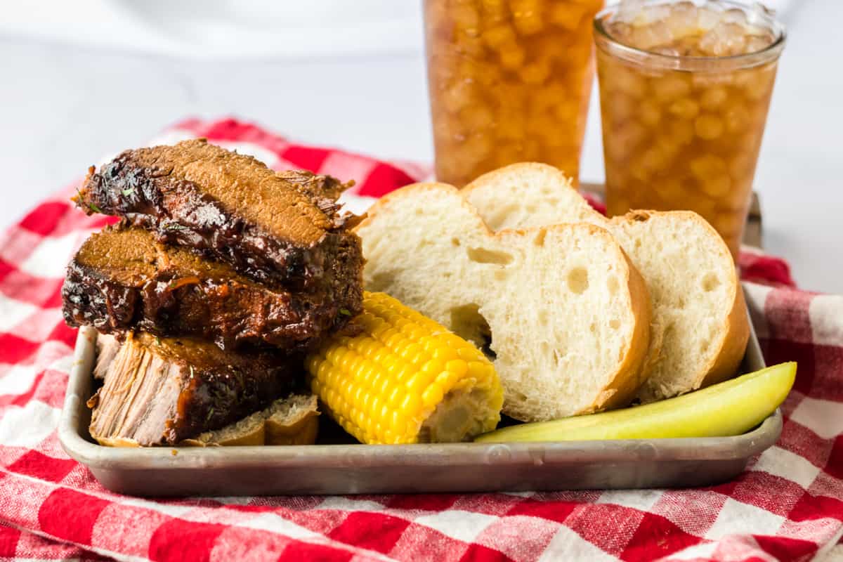 Slow Cooker BBQ Brisket with corn on the cob, bread, pickle, and iced tea.