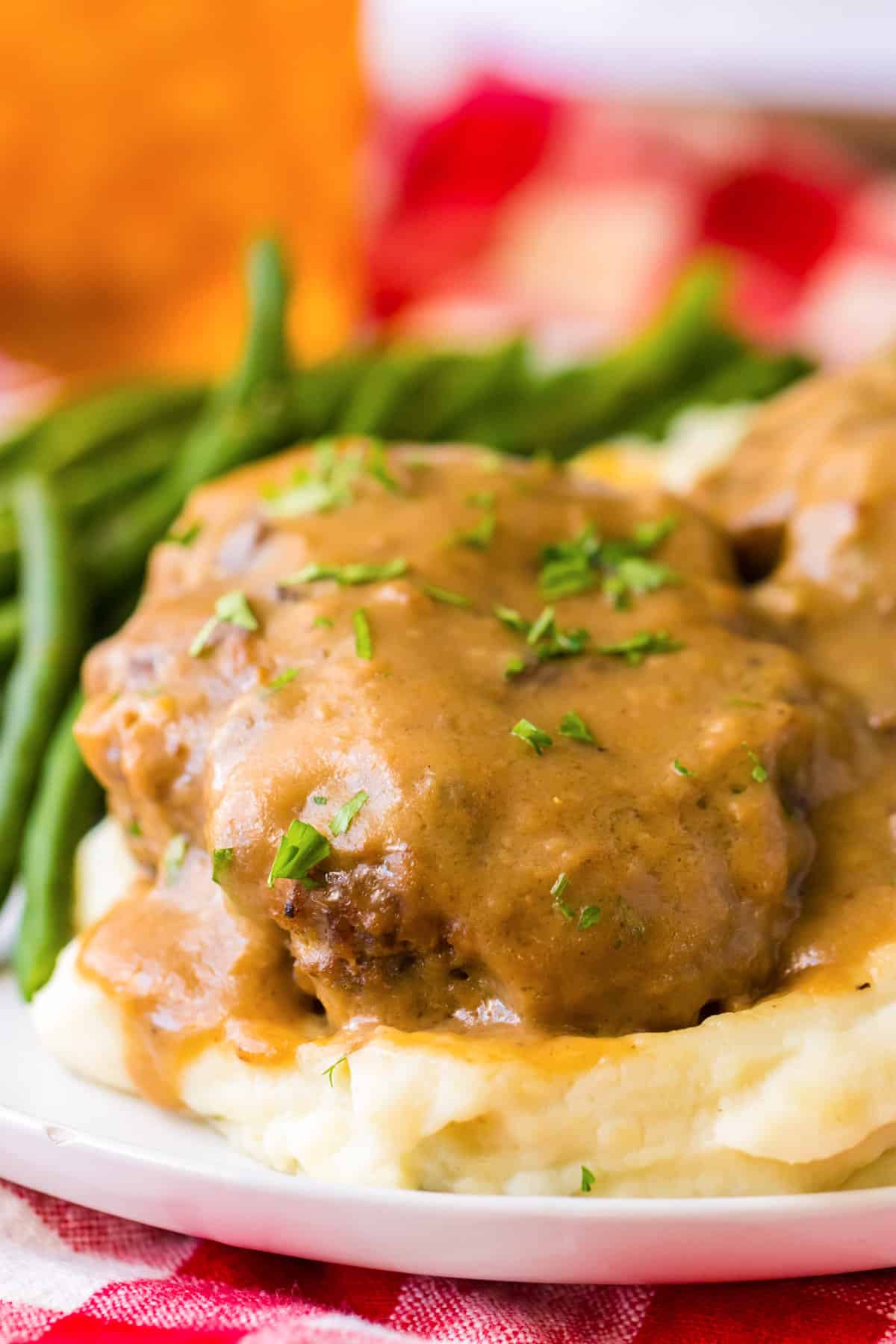 Side view of thick hamburger steak sitting on a bed of mashed potatoes and covered with brown gravy.